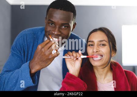 Felice coppia diversa nel spazzolare i denti in bagno, guardando la fotocamera sorridente Foto Stock