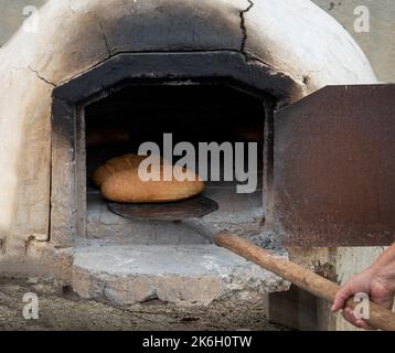 Pane fresco fatto in casa cotto in un forno tradizionale di argilla. Persona che tiene il bastone con il pane Foto Stock