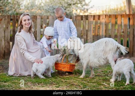 Mamma con una bambina nutre una capra. Donna con bambini in fattoria. Famiglia con capre. Vita di villaggio. Foto Stock