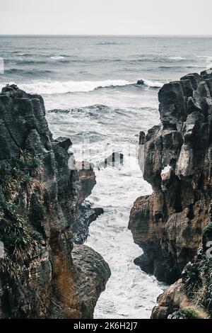 sea ​​waves si schiantano in uno spazio tra le grandi rocce in una giornata di cattivo tempo con mari e nuvole all'orizzonte, rocce pancake, nuova zelanda Foto Stock