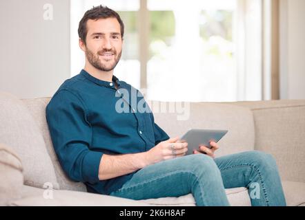 Ive ha tutto ciò di cui ho bisogno per un weekend rilassante. Ritratto corto di un bel giovane uomo che usa il suo tablet mentre si siede sul divano a casa. Foto Stock