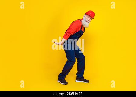 Foto a tutta lunghezza di un caposquadra positivo ottimista con barba bianca e casco rosso resistenza peso pesante isolato su sfondo giallo Foto Stock