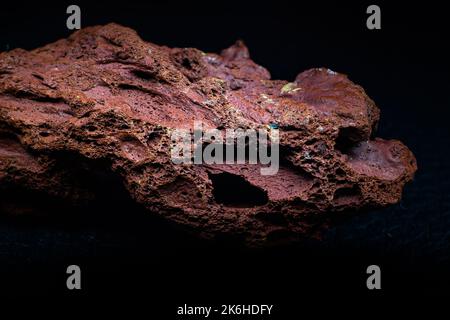 Rosso ruvido pietra lavica macro focalizzata e isolata su superficie nera isolata Foto Stock
