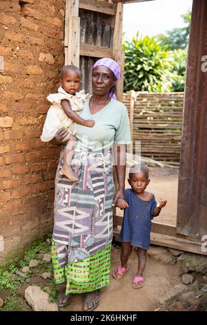 Sylvia Katehero (60) partecipa al progetto reale della LWR (economie rurali e mezzi di sussistenza agricoli) in Kasese, Uganda. Qui, lei si trova con sua nipote, Eva (2, L), e nipote, Edwin (2, R), fuori casa. Sylvia e suo marito vivono con cinque nipoti, tutti di età compresa tra i due e i cinque anni. Prima dell'inizio del progetto, non era in grado di prendersi cura adeguatamente dei nipoti e molti di loro erano malnutriti e spesso si ammalavano. Ci sono stati momenti in cui i bambini erano così malati che temeva per la loro vita. Perché vive così lontano da una struttura sanitaria, e. Foto Stock