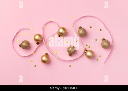 Biglietto di Natale con palline dorate, coriandoli a forma di cuore e nastro di raso su sfondo rosa con luci sfocate bokeh Foto Stock