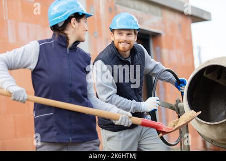 costruttori femminili e maschili che utilizzano betoniera e pala Foto Stock