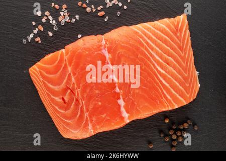 Un pezzo di filetto di salmone fresco con sale su pietra ardesia, macro, vista dall'alto. Foto Stock