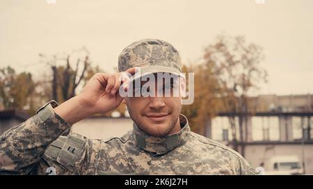 Sorridente soldato in uniforme cappuccio di regolazione e guardare la telecamera all'aperto, immagine stock Foto Stock
