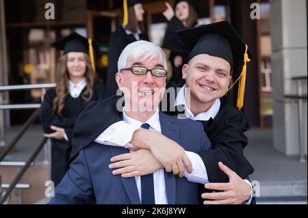 Padre e figlio si abbracciano alla laurea. Il genitore si congratula con il laureato. Foto Stock