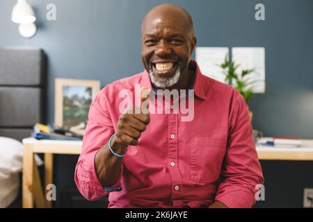 Felice uomo afroamericano senior fare videochiamata sorridendo e dando pollice su segno alla fotocamera Foto Stock