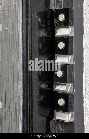 Set di quattro vecchie campane bianche e nere con nomi all'esterno di un edificio di appartamenti Foto Stock