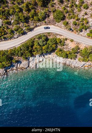 Ripresa aerea verticale del pick-up che si muove lungo la strada curva vicino al mare tranquille onde sulla costa dell'isola greca di Cefalonia. Trasporto, viaggio Foto Stock