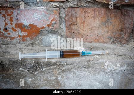 Siringa con una sostanza narcotica, sullo sfondo di una parete abbandonata. Concetto di dipendenza. Foto Stock