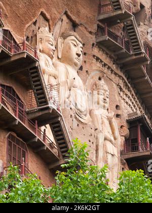 Scale e gravità sfidando l'alto passaggio / scale e passaggi collegati alla parete rocciosa a strapiombo ha permesso ai visitatori di stretto contatto con le figure di argilla e le antiche sculture in pietra. Il sito di rappresentazioni buddhiste / figure raffigurazioni e immagini del Buddha (alcune sembrano essere state recentemente restaurate utilizzando cemento) sulla parete rocciosa delle grotte di Maijishan, precedentemente romanizzate come Maichishan, una serie di 194 grotte tagliate sul lato delle montagne di Majishan a Tianshui, provincia di Gansu, Cina. PRC. (67/126) Foto Stock