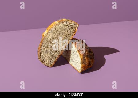 Delizioso pane fatto in casa con semi di papavero minimalista su un tavolo di colore viola. Pane affettato a metà. Foto Stock