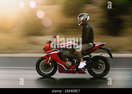 Uomo che guida una motocicletta da corsa di colore rosso senza mani sull'autostrada. Foto Stock