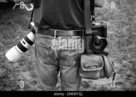 Un fotografo di giornale con fotocamere Canon e una borsa per fotocamera Domke scatta fotografie in un festival all'aperto a Santa Fe, New Mexico. Foto Stock