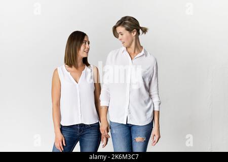 Amici felici che si divertono su sfondo bianco. Due fidanzate in piedi che indossano maglietta bianca e jeans Foto Stock