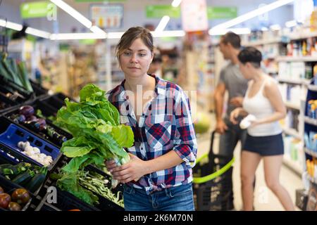 Donna che sceglie lattuga in supermercato Foto Stock