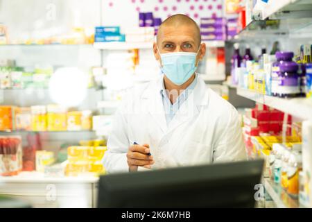 Ritratto del farmacista in maschera medica lavorando al registratore di cassa in farmacia Foto Stock