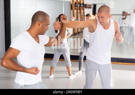 Uomini che praticano le mosse di base durante il corso di autodifesa in palestra Foto Stock