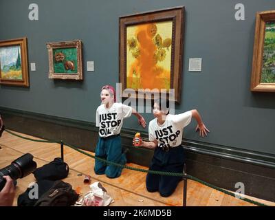 Londra, Regno Unito. 14th Ott 2022. Una foto dell'handout pubblicata dal gruppo Just Stop Oil mostra due manifestanti che hanno gettato una zuppa al famoso 1888 di Vincent Van Gogh Girasoli alla National Gallery di Londra venerdì, ma non ha causato danni al dipinto ricoperto di vetro. Il gruppo Just Stop Oil, che vuole che il governo britannico interrompesse nuovi progetti nel settore del petrolio e del gas, ha affermato che gli attivisti hanno scaricato due lattine di zuppa di pomodoro sulla pittura a olio, una delle opere più iconiche dell'artista olandese. I due manifestanti si incollarono anche alla parete della galleria. Credit: ZUMA Press, Inc./Alamy Live News Foto Stock