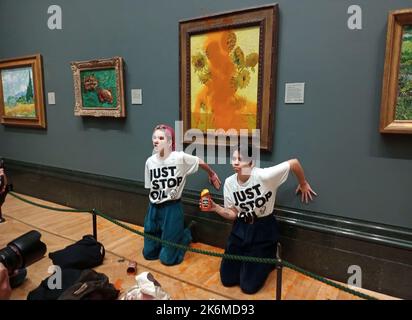 Londra, Regno Unito. 14th Ott 2022. Una foto dell'handout pubblicata dal gruppo Just Stop Oil mostra due manifestanti che hanno gettato una zuppa al famoso 1888 di Vincent Van Gogh Girasoli alla National Gallery di Londra venerdì, ma non ha causato danni al dipinto ricoperto di vetro. Il gruppo Just Stop Oil, che vuole che il governo britannico interrompesse nuovi progetti nel settore del petrolio e del gas, ha affermato che gli attivisti hanno scaricato due lattine di zuppa di pomodoro sulla pittura a olio, una delle opere più iconiche dell'artista olandese. I due manifestanti si incollarono anche alla parete della galleria. Credit: ZUMA Press, Inc./Alamy Live News Foto Stock