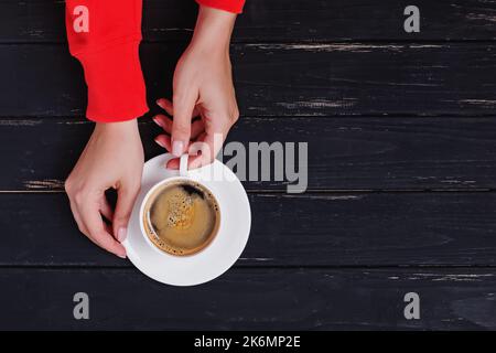 Mani femminili in felpa rossa che tiene una tazza di caffè caldo fresco, vista dall'alto, spazio copia Foto Stock