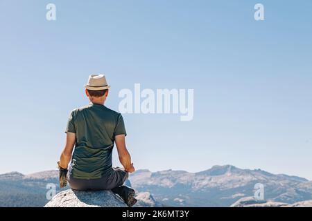 Uomo meditato in montagna. Vista dal retro. Concetto di consapevolezza. Foto Stock