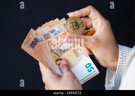 Mani di closeup donna che tengono monete d'oro di cripto e banconote in euro, indossando una giacca bianca. Foto Stock