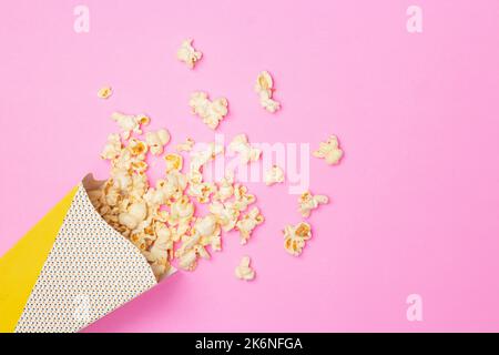 Concetto snack, popcorn dolce galleggiano fuori dalla tazza di carta su sfondo rosa. Foto Stock