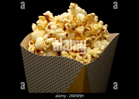 Spuntino di guardare il concetto di film, popcorn dolce in tazza di carta su sfondo nero. Foto Stock