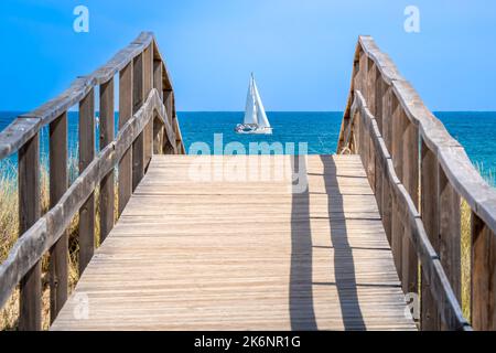 Un ponte pedonale in legno costruito su una duna di sabbia dà accesso alla spiaggia di Meia Praia nella destinazione turistica Lagos in Portogallo con barca a vela. Foto Stock