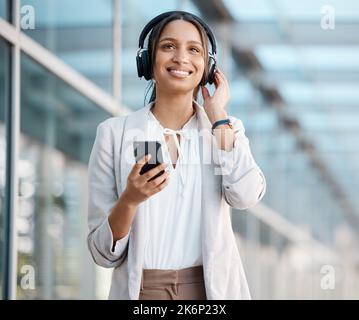 Donna, smartphone e cuffie che ascoltano musica, radio o podcast in pausa nel paesaggio urbano. Giovane professionista, persona d'affari e streaming online Foto Stock