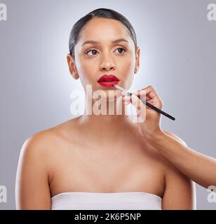 Dipingere il rosso città. una giovane donna attraente in piedi in studio, mentre un artista trucco applica rossetto. Foto Stock
