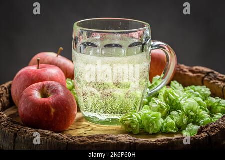 Birra di sidro fresco e frizzante con luppolo, mele e frumento su vecchio barile di legno Foto Stock