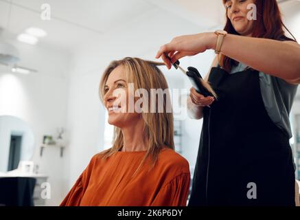 Salone, taglio di capelli e stile con una cliente donna raddrizzando i capelli per la bellezza o il benessere. Moda, cliente e capelli con una parrucchiera o Foto Stock