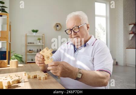 L'uomo anziano addestra le abilità motorie fini per la demenza o la malattia di Alzheimer assemblando i puzzle di legno Foto Stock