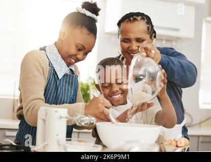 Continuare a mescolare. una nonna che cuoce con i suoi due nipoti a casa. Foto Stock