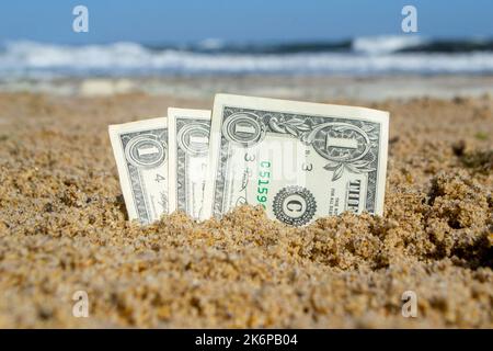 Carta fattura un dollaro sepolto nella sabbia sulla spiaggia sullo sfondo del mare primo piano. Banconote in denaro americane di un dollaro di denominazione in sabbia nella giornata estiva di sole. Concetto di finanza monetaria Foto Stock