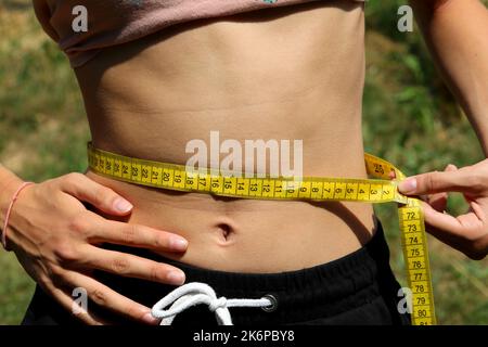 la giovane ragazza skinny misura la sua stretta linea di vita con un flessibile metro giallo durante il digiuno Foto Stock