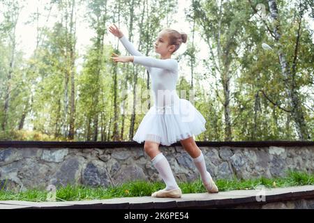 una piccola ballerina mostra elementi di coreografia in una giornata estiva su un sentiero nel parco Foto Stock