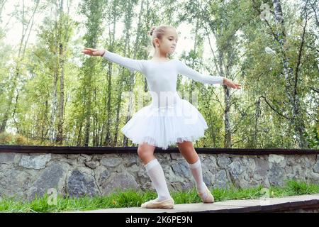 una piccola ballerina mostra elementi di coreografia in una giornata estiva su un sentiero nel parco Foto Stock