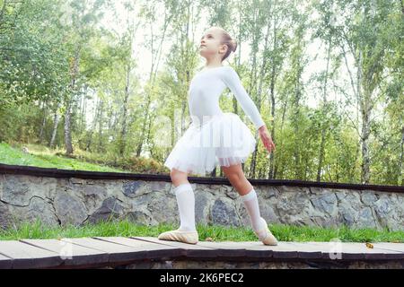 una piccola ballerina mostra elementi di coreografia in una giornata estiva su un sentiero nel parco Foto Stock