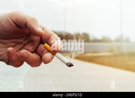 La mano dell'uomo tiene una sigaretta accesa. Le sigarette sono nocive per la salute Foto Stock