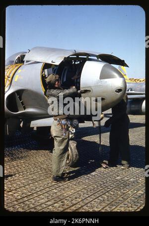 Vista frontale a metà destra del naso di una Lockheed F-80C Shooting Star (s/n 47-555) recante le marcature del 80th Fighter Bomber Squadron (FBS), da qualche parte in Corea. Due dei pannelli sul naso sono aperti, e due crewmen a terra caricano le pistole con munizioni calibro .50. Una scala è montata contro il fianco dell'aereo, che conduce al pozzetto. Sullo sfondo, una parte della fusoliera posteriore e della coda di un'altra F-80C Shooting Star è visibile (s/n 49-740). Dietro questo velivolo appaiono dei sandbags. Foto Stock