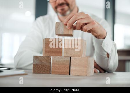 Ive ha preso in considerazione il futuro. un uomo d'affari irriconoscibile seduto da solo nel suo ufficio e utilizzando blocchi da costruzione per pianificare. Foto Stock