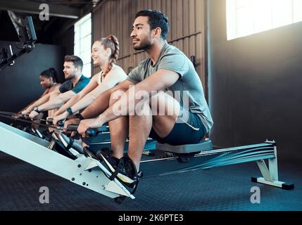 Questa macchina separa il debole dal forte. Spettacolo di un gruppo di persone che si remano insieme in palestra. Foto Stock