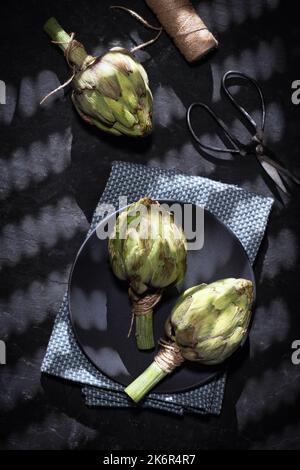 Carciofi viola crudi su sfondo nero Foto Stock