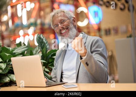 Buon vecchio uomo d'affari che celebra i buoni risultati vincendo i soldi dalla scommessa in linea. Foto Stock